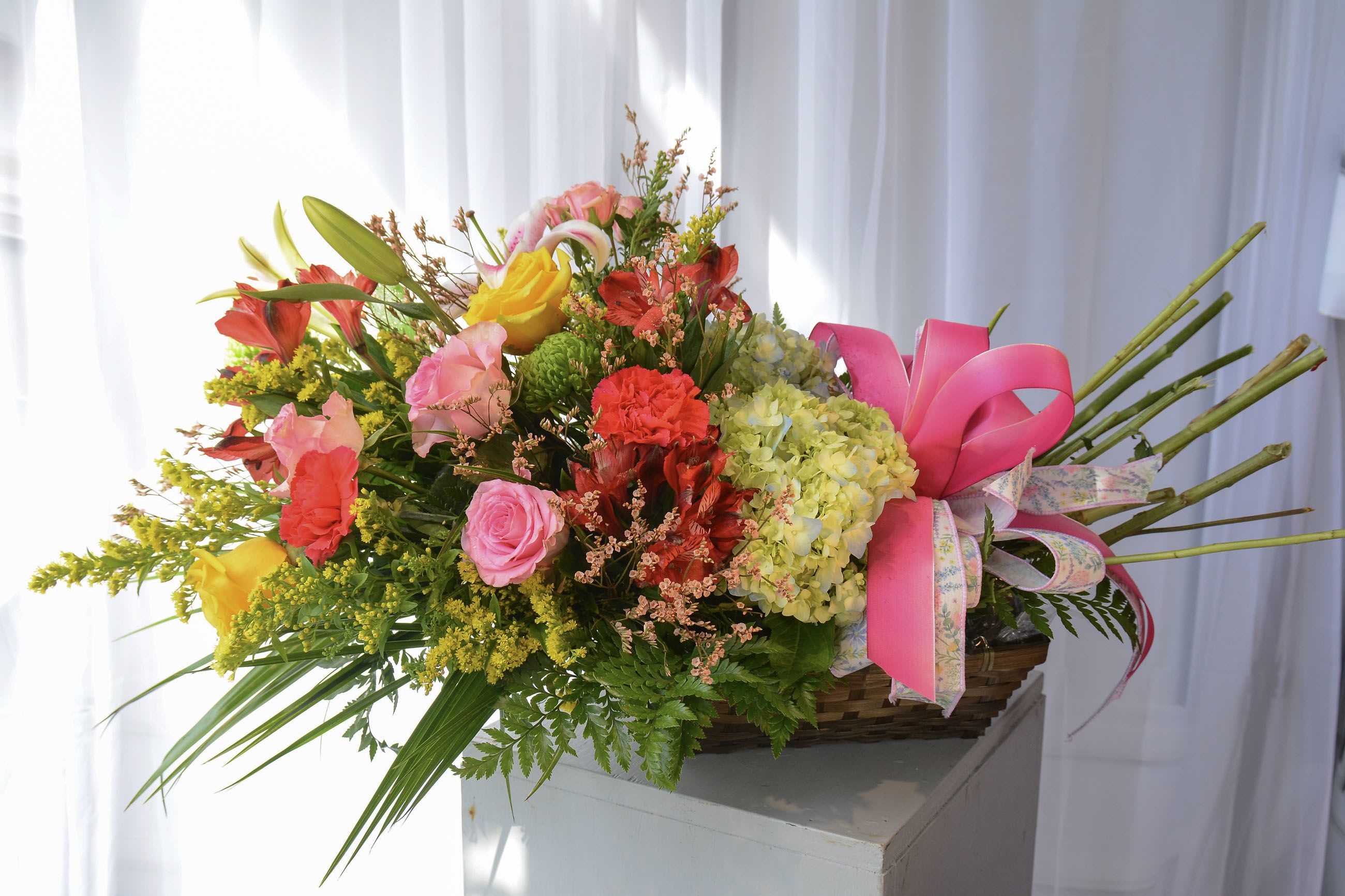 Colorful mixed flower arrangement in a basket with pink ribbon