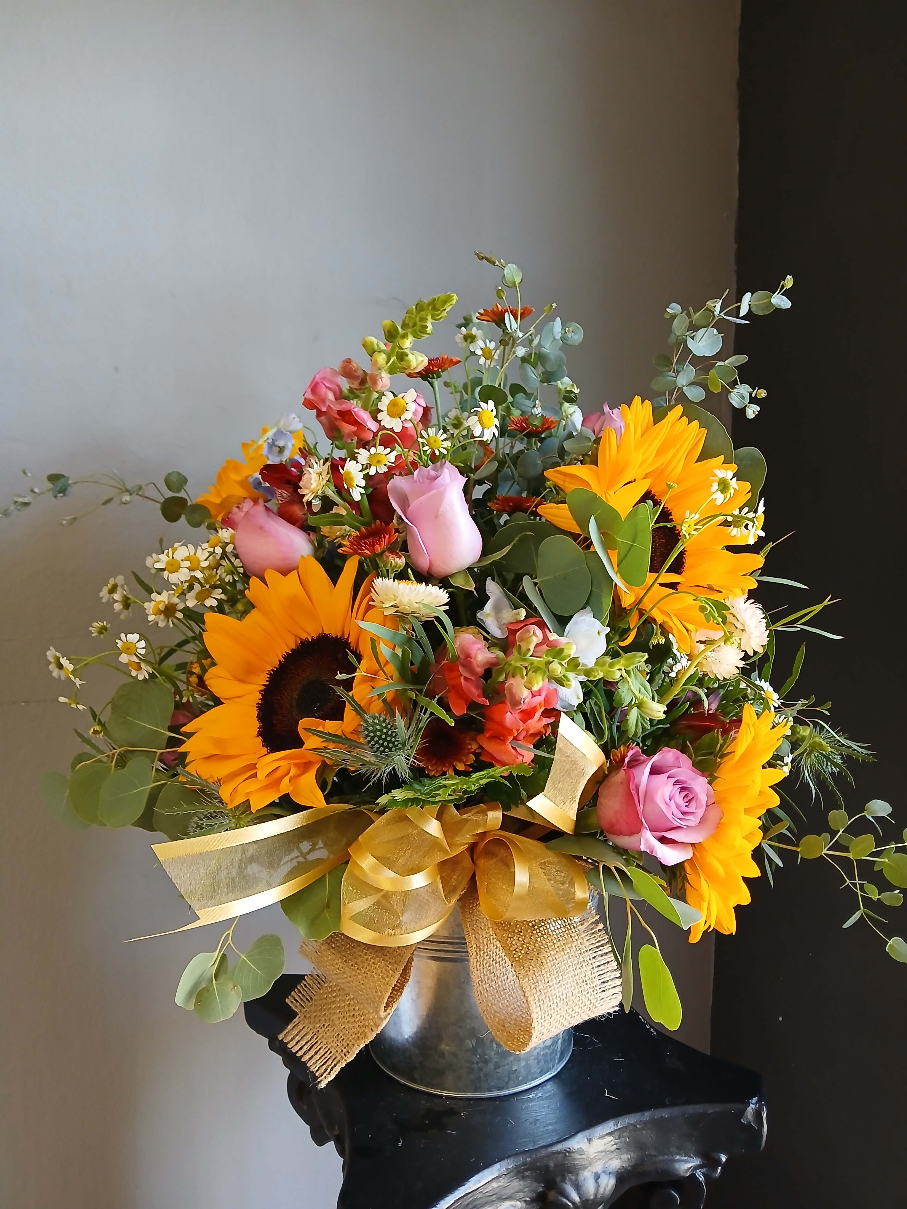 Mixed bouquet with sunflowers, pink roses, and daisies in a metal bucket