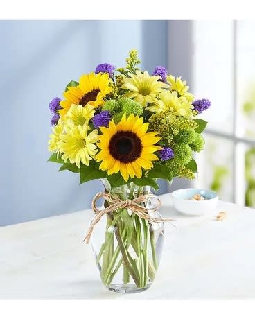 Sunflowers and yellow daisies in a clear glass vase with a twine bow