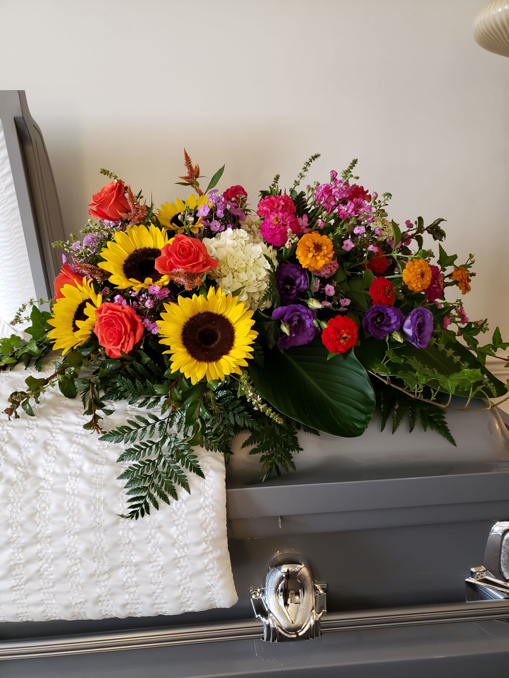 Bright mixed flower spray on a casket with sunflowers, roses, and purple blooms