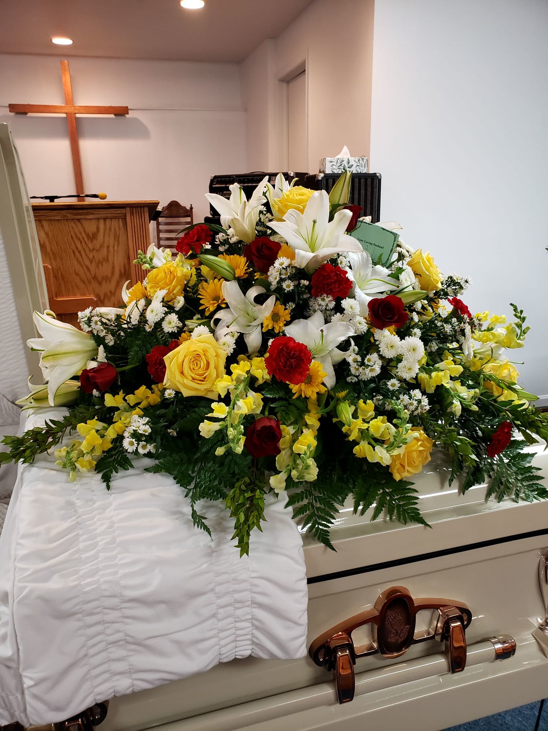 Large casket spray with white lilies, red and yellow roses, and yellow flowers