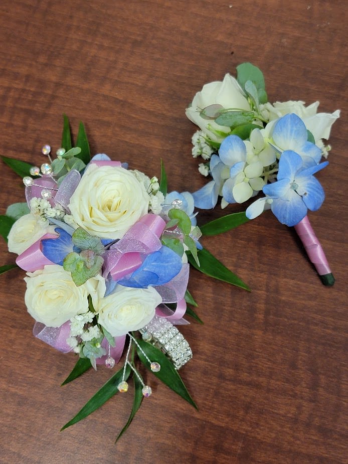Two small floral bouquets with white roses and blue hydrangea accents on a wooden surface.