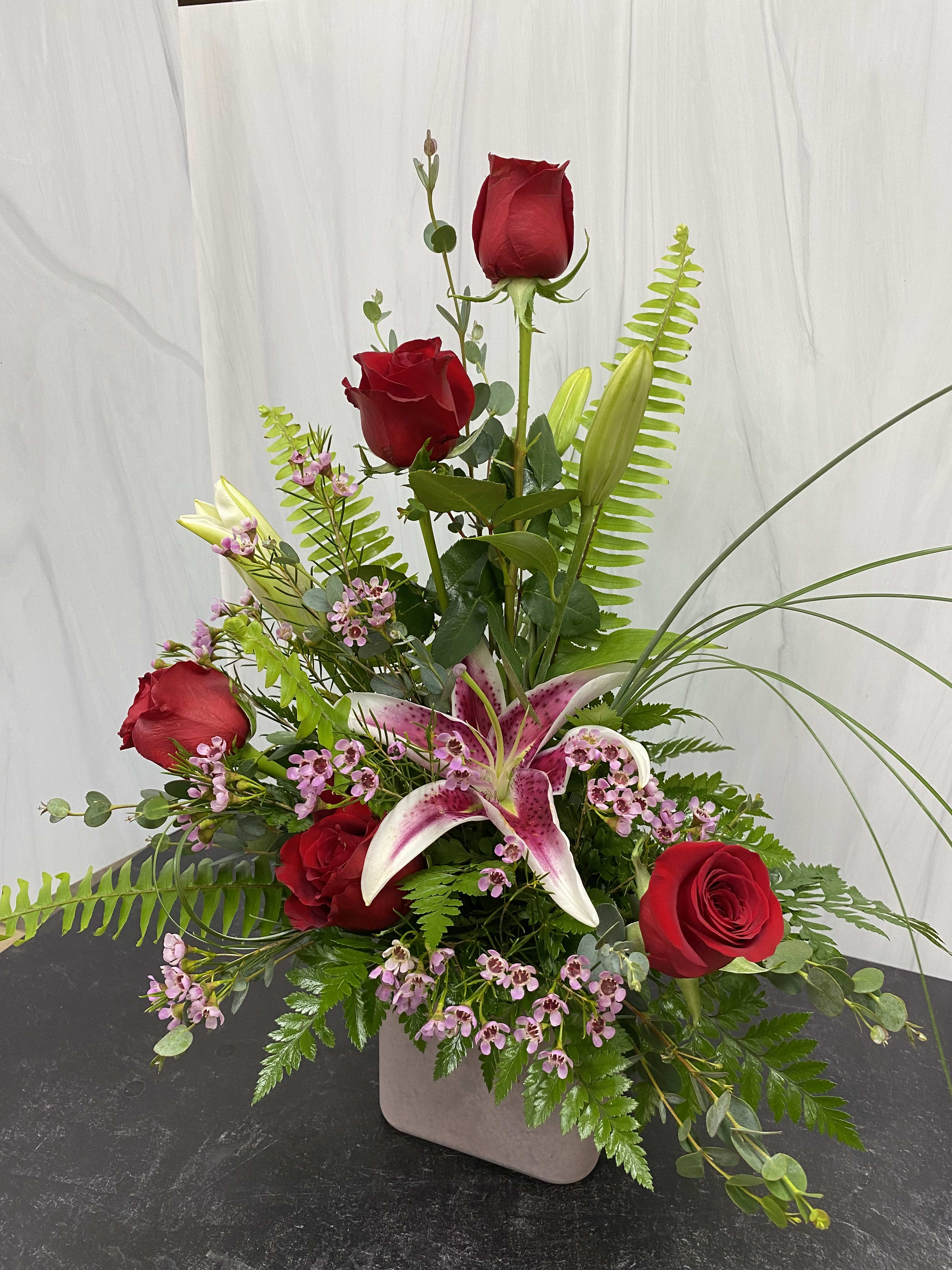 Tall arrangement of red roses and a pink stargazer lily in a square vase