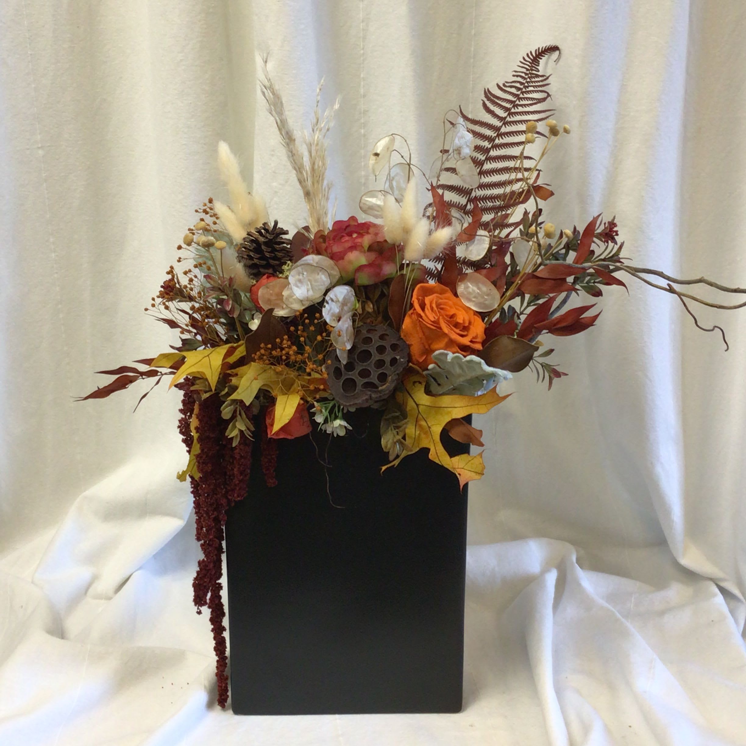 Autumn floral arrangement in a black rectangular vase with orange roses and dried accents