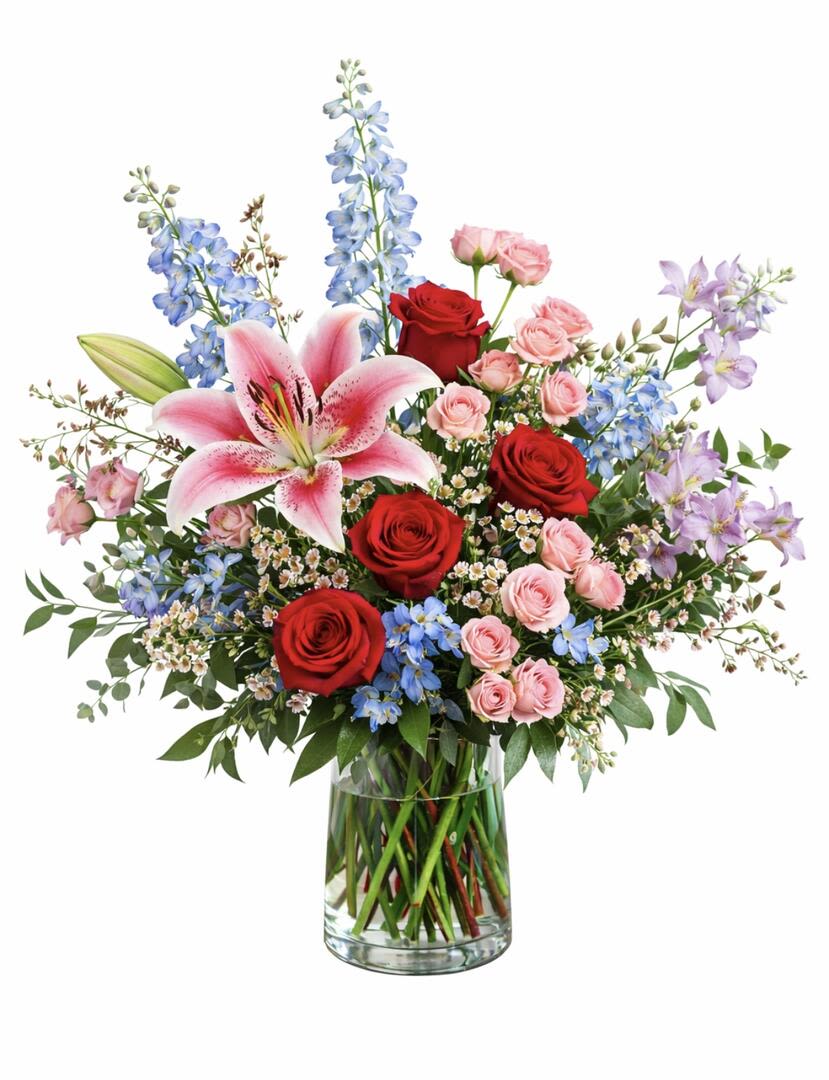 Bouquet of red and pink roses with lilies and blue flowers in a glass vase