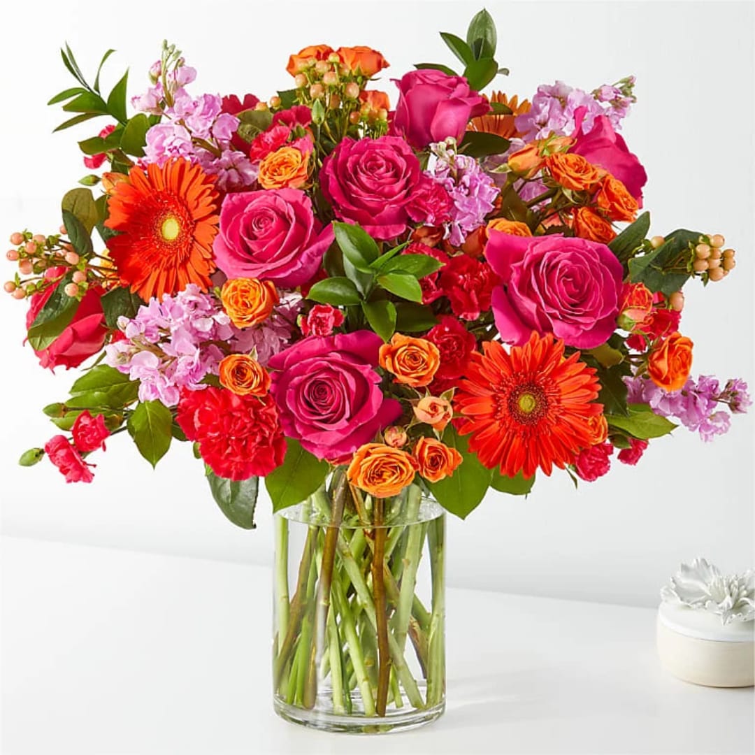 Mixed bouquet of pink, orange, and red flowers in a clear glass vase