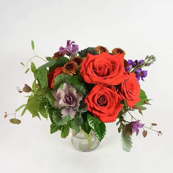 Red roses and purple flowers in a clear glass vase