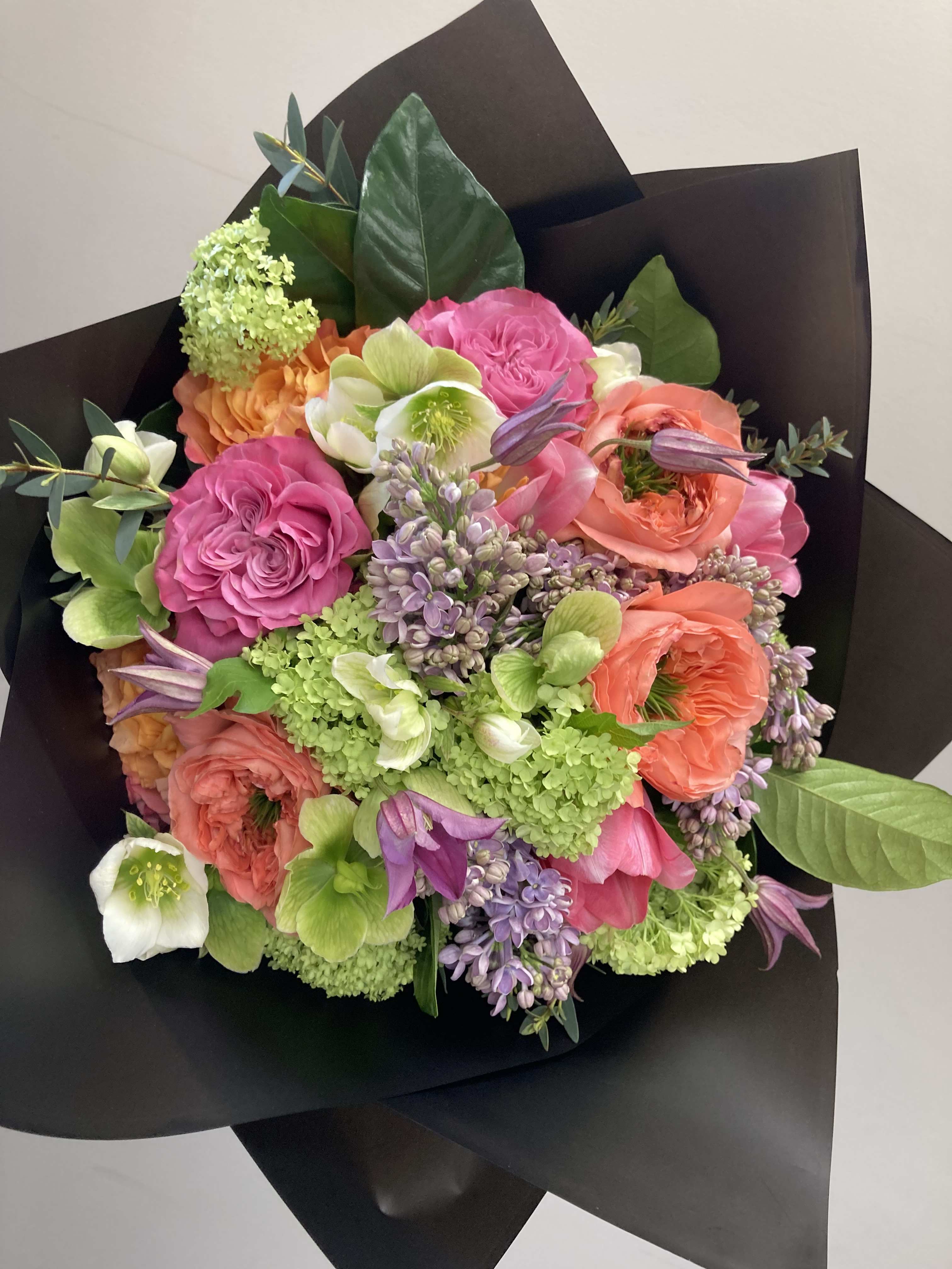 Mixed bouquet of pink, coral, and green flowers wrapped in black paper