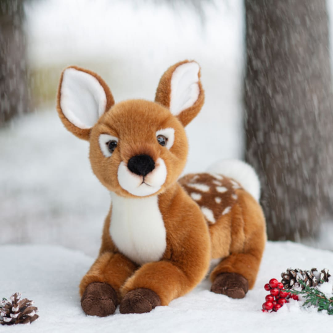 Plush deer toy sitting in snow with pinecones and red berries