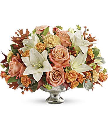 Peach roses and white lilies arranged in a silver pedestal vase
