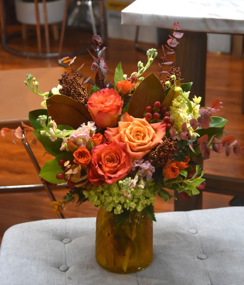 Autumn-toned bouquet of orange roses and mixed blooms in an amber glass jar vase