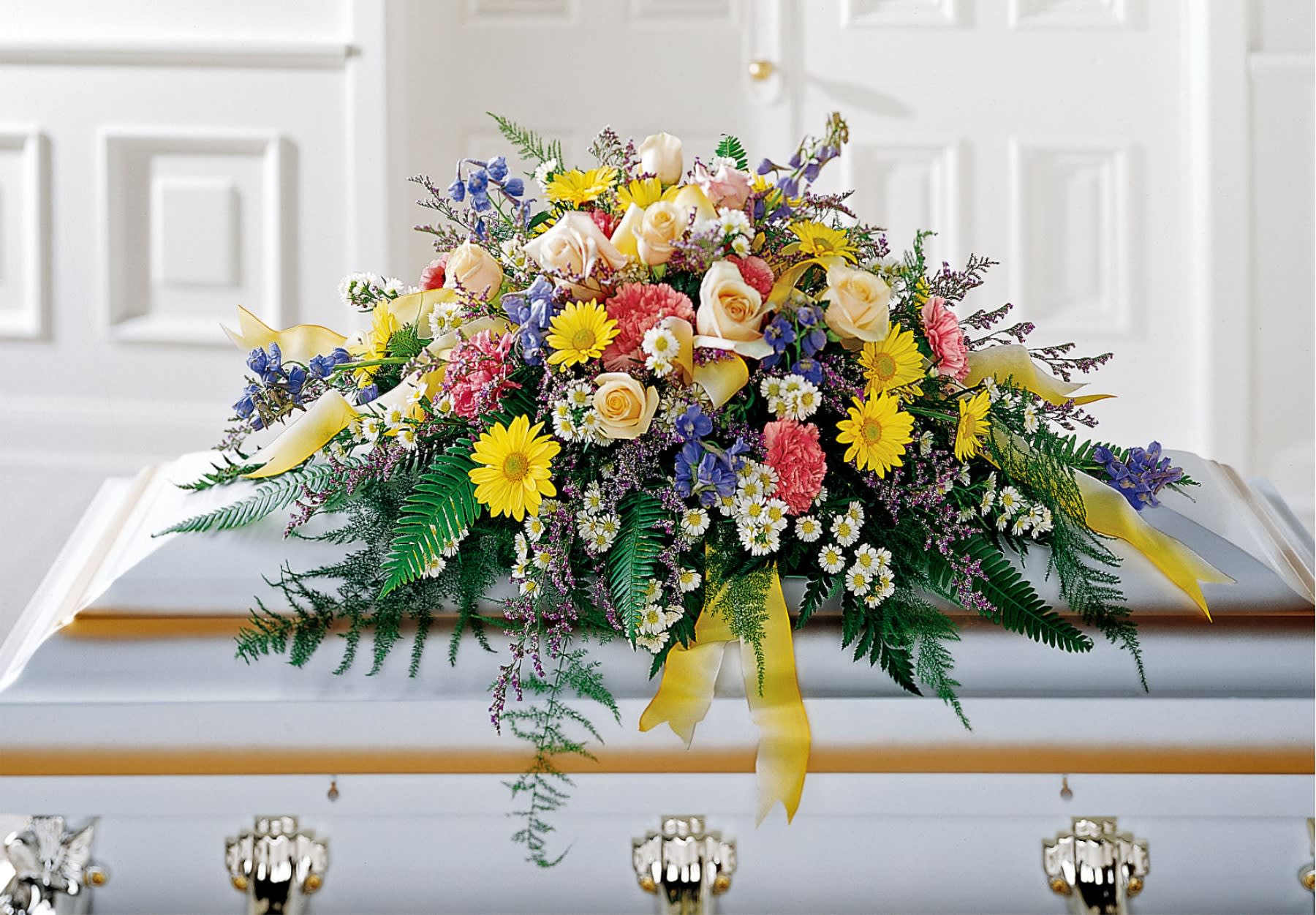 Colorful floral casket spray with roses, daisies, and ribbons