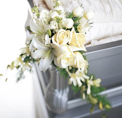 White floral bouquet with roses and lilies draped over a gray casket