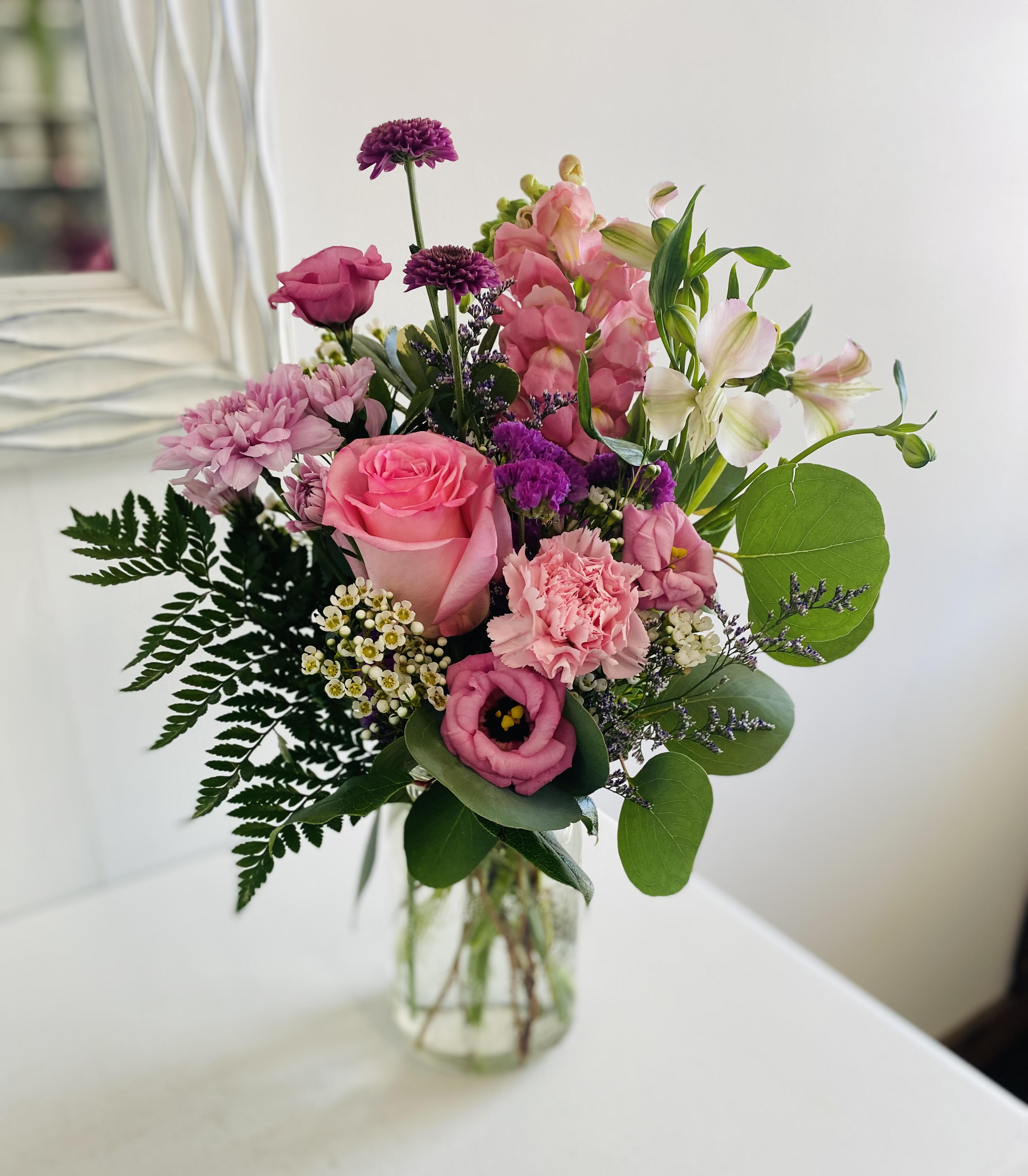 Mixed bouquet of pink and purple flowers with white accents in a clear glass jar vase
