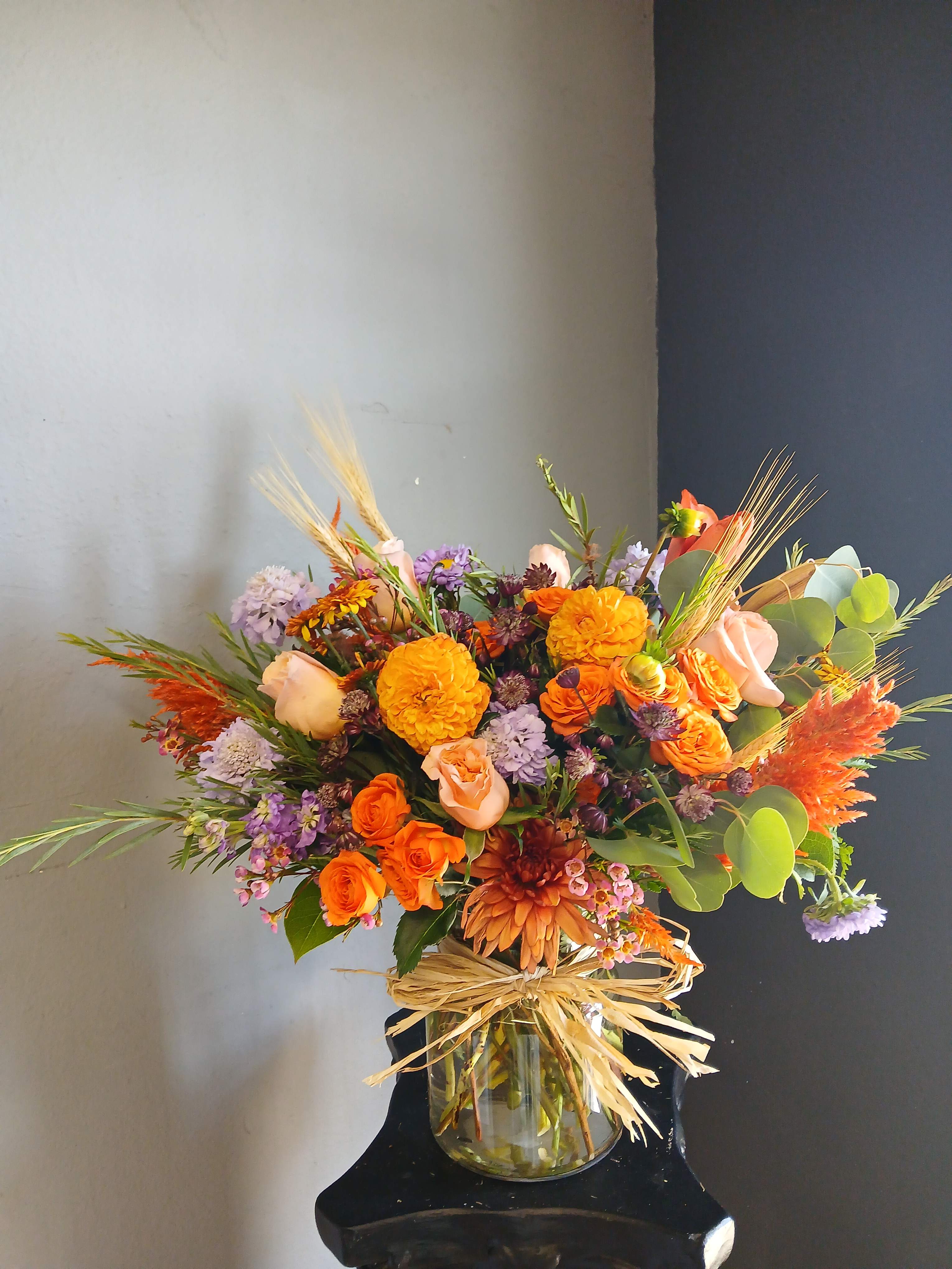 Orange and lavender mixed bouquet in a glass vase with raffia bow