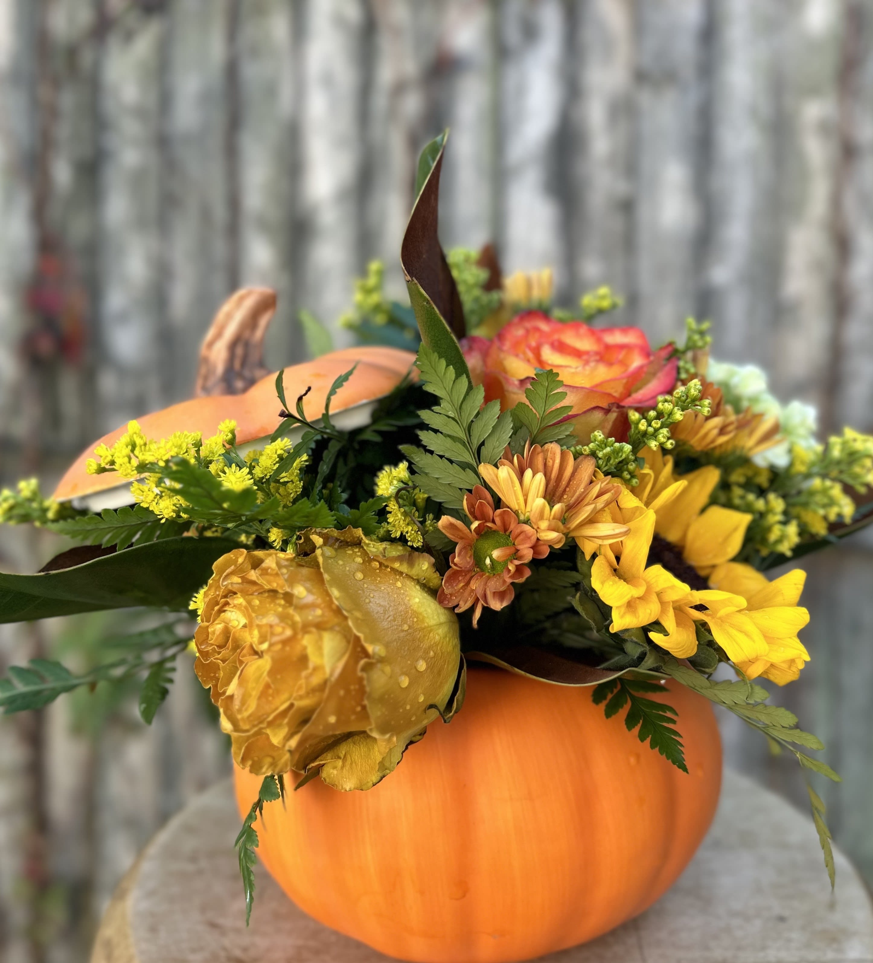 Fall flower arrangement in a pumpkin container with yellow and orange blooms