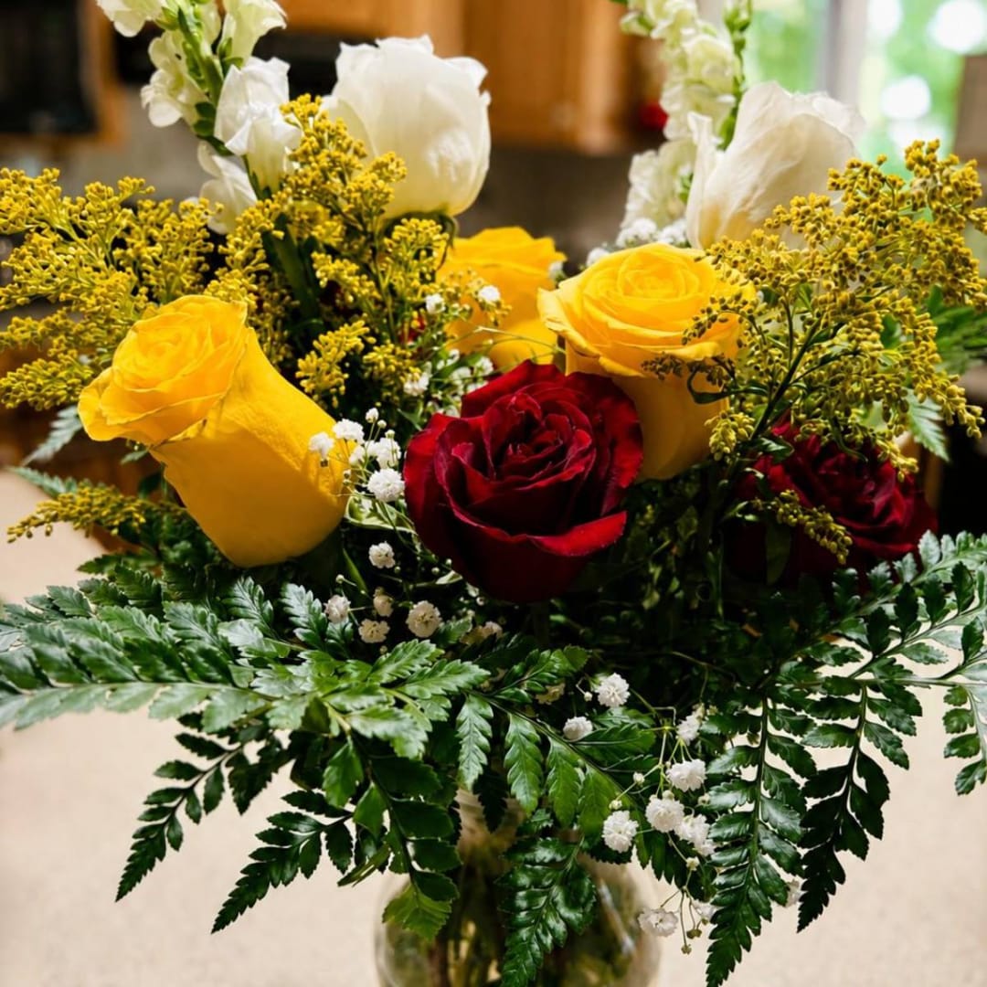 Bouquet of red and yellow roses with white flowers in a glass vase