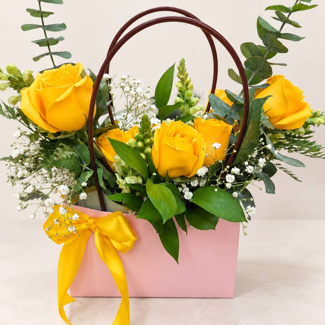Yellow roses arranged in a pink gift bag with a ribbon bow