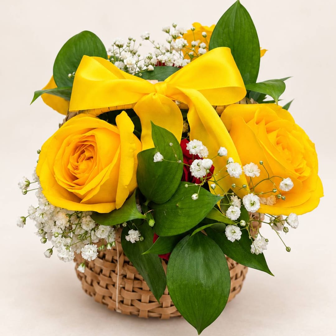 Yellow roses in a woven basket with a large yellow ribbon