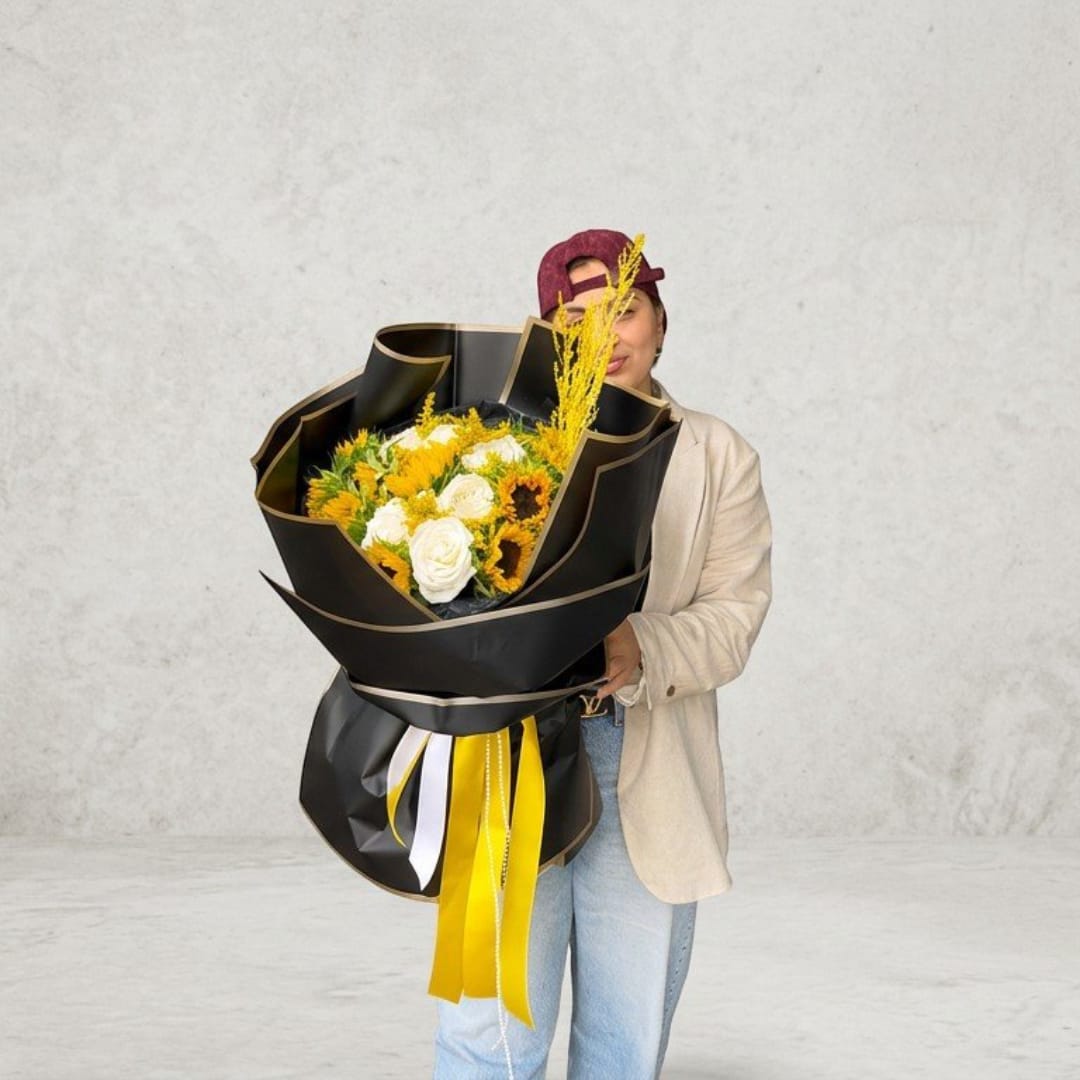 Person holding a large bouquet of white and yellow flowers wrapped in black paper