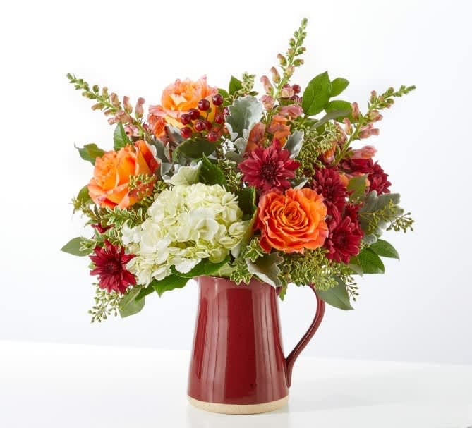 Mixed bouquet of orange, red, and white flowers in a red pitcher vase