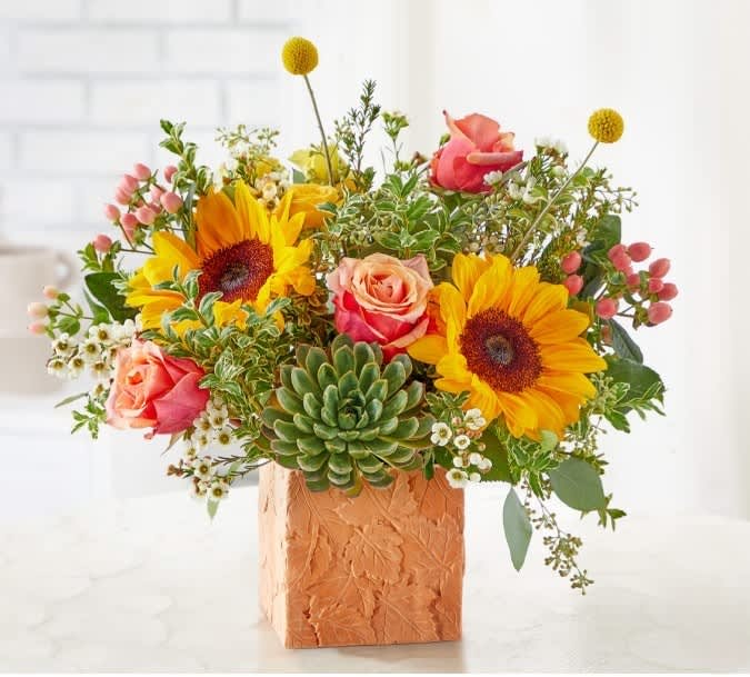Mixed bouquet with sunflowers, roses, and a succulent in a textured square vase