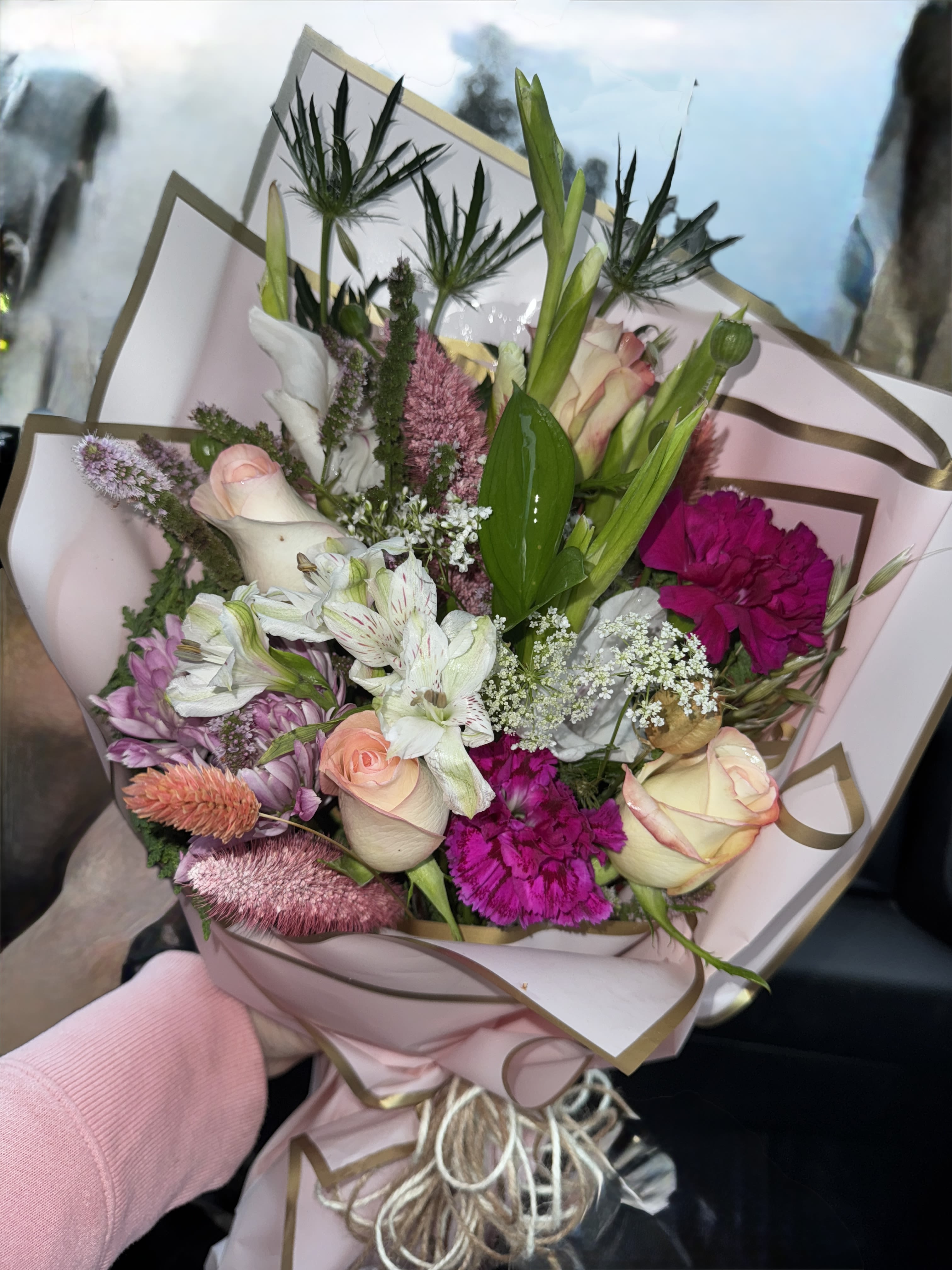 Hand-tied bouquet of pink, white, and magenta flowers wrapped in blush paper