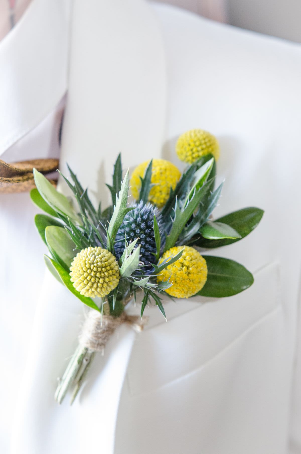 Thistle &amp; Gold Bout - A fresh, textural boutonniere featuring bold blue thistle and golden billy balls, accented with sleek greenery and finished with a natural wrap.
