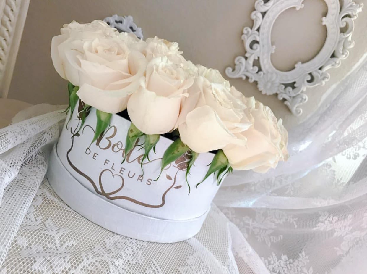 Cream roses arranged in a white hat box with lace fabric