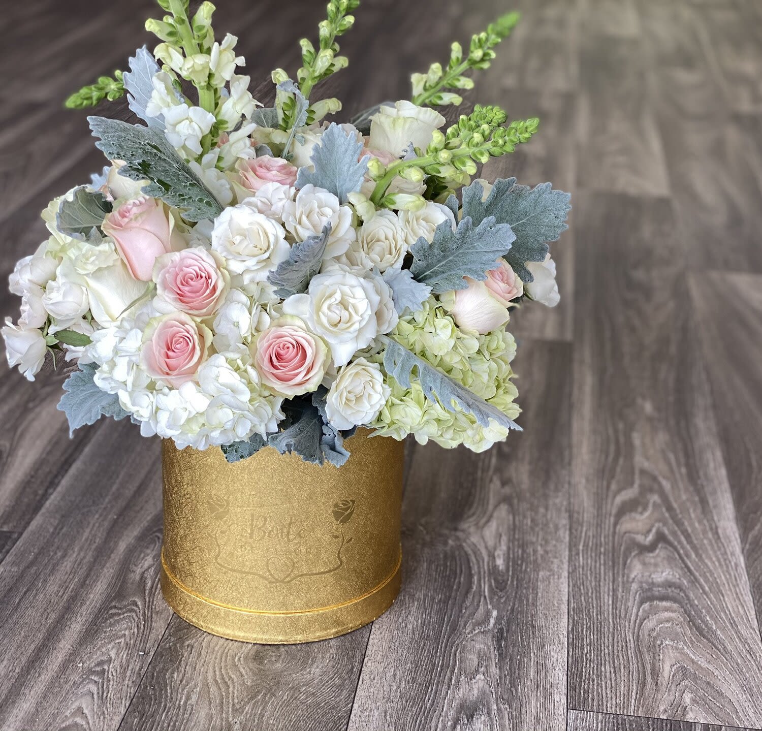 Pink and white roses arranged in a gold round box