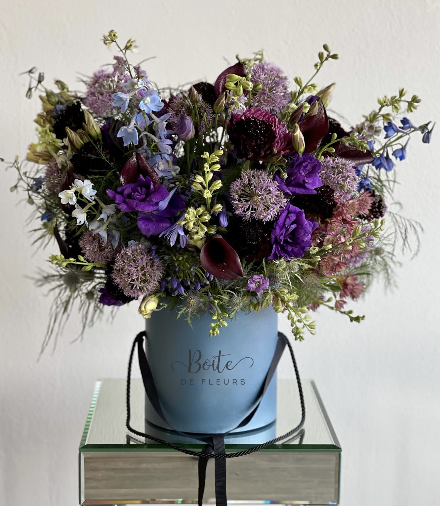 Purple and blue mixed bouquet in a blue hatbox with black ribbon handles