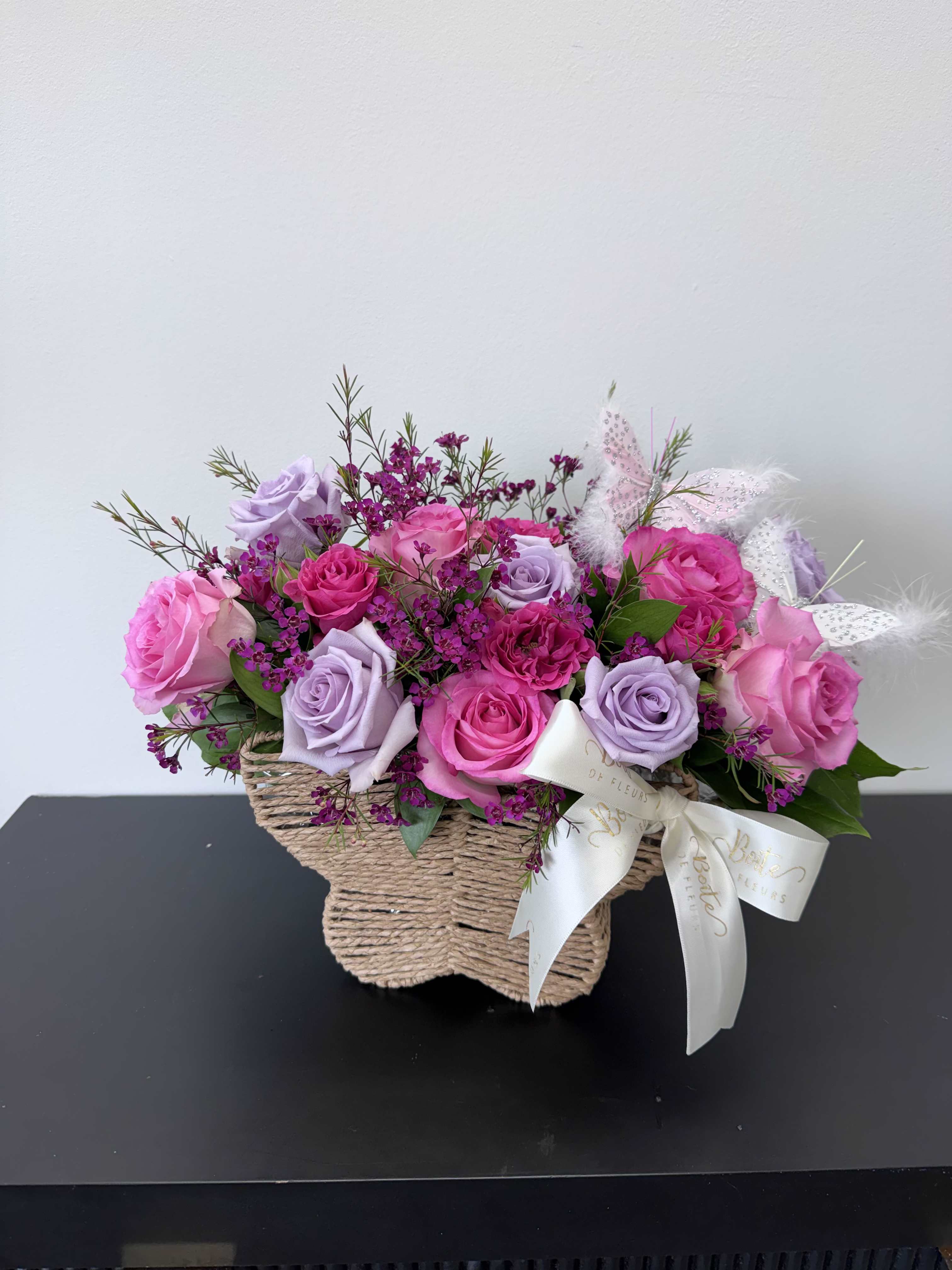 Pink and lavender roses in a woven basket with a ribbon bow