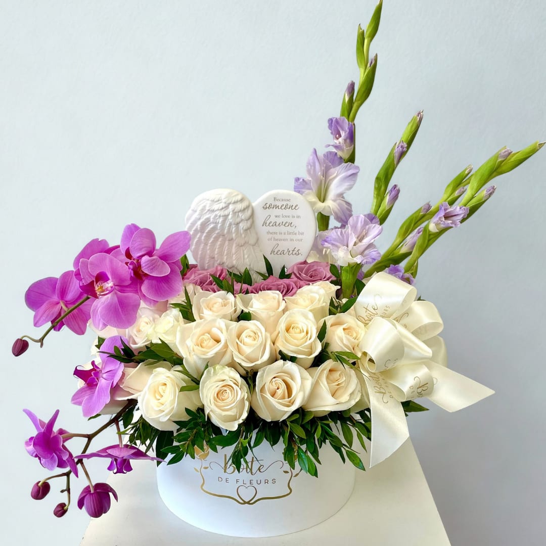 White roses and purple orchids arranged in a round hat box with a ribbon