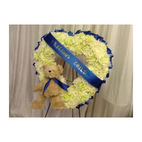 Heart-shaped white floral wreath with a teddy bear and blue ribbon
