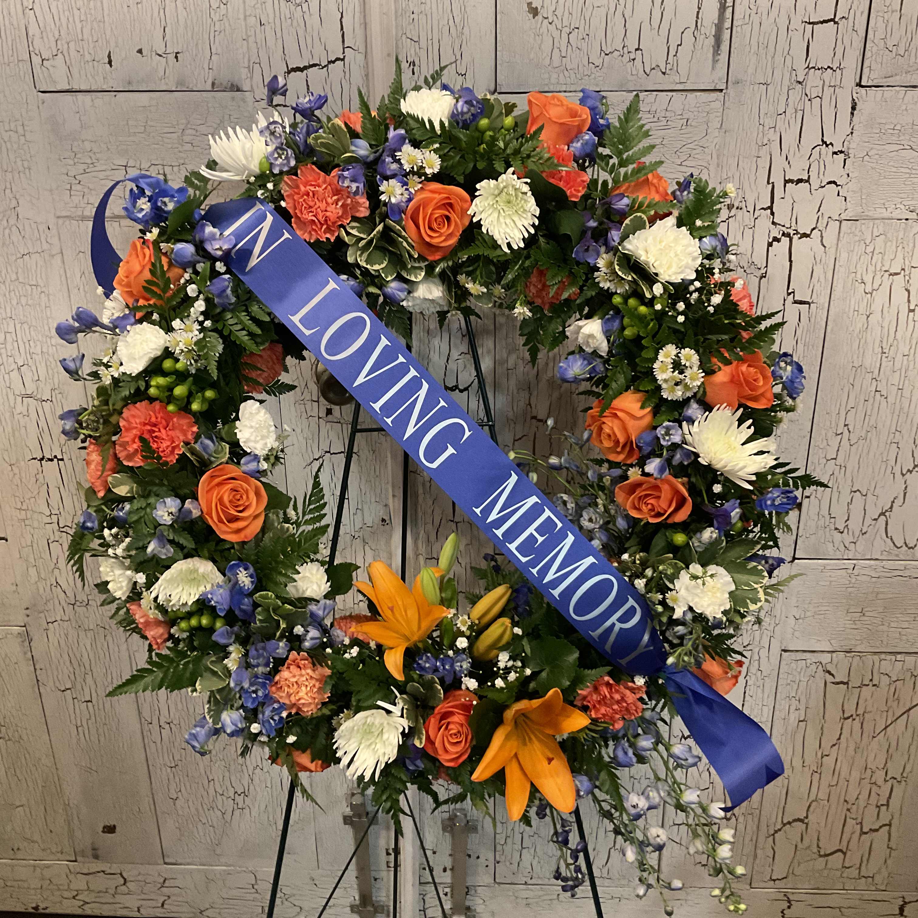 Floral memorial wreath with a blue ribbon reading "IN LOVING MEMORY"