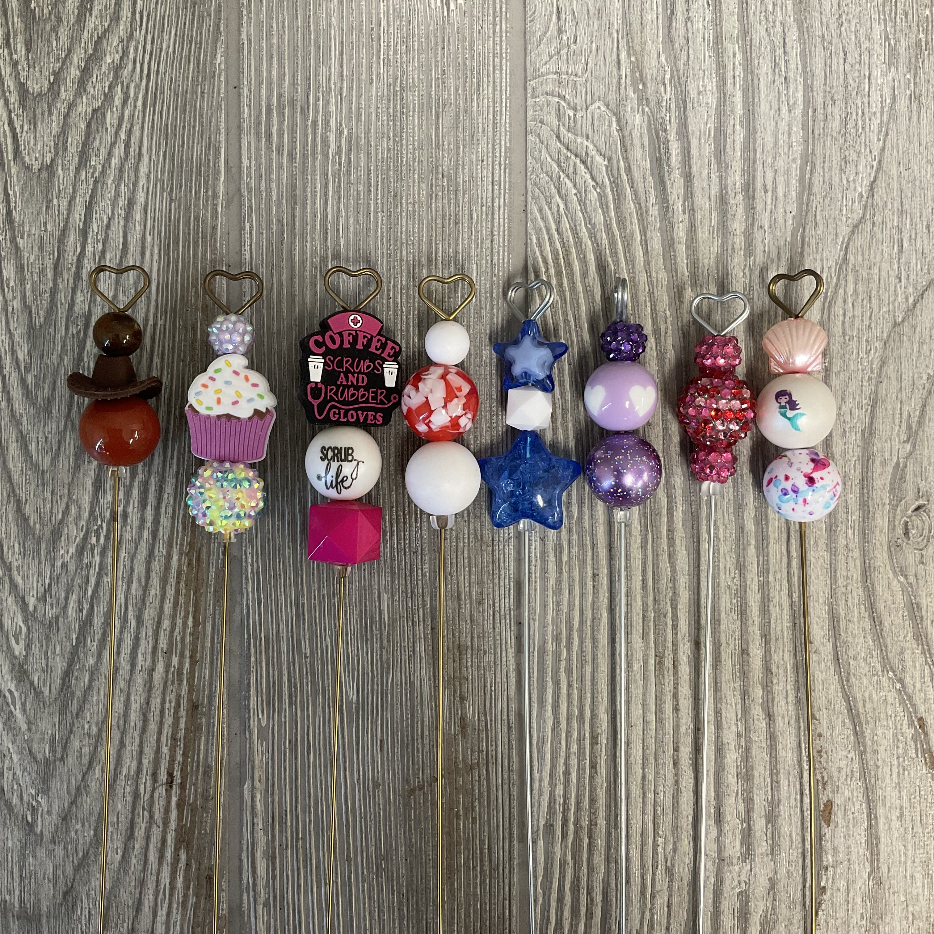Decorative beaded picks with heart-shaped toppers arranged on a wood surface.