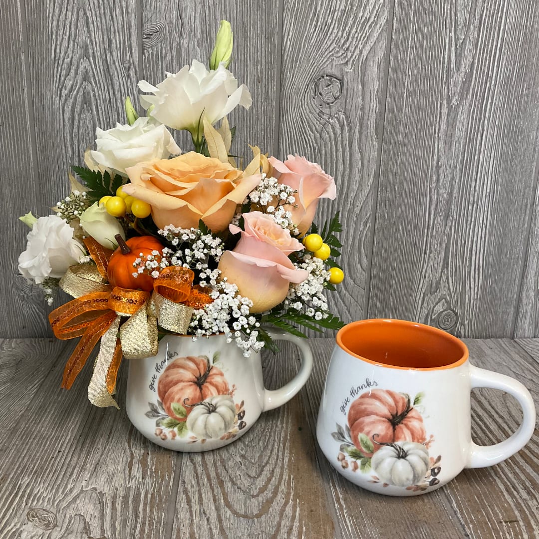 Pumpkin-themed floral arrangement in a mug beside a matching mug