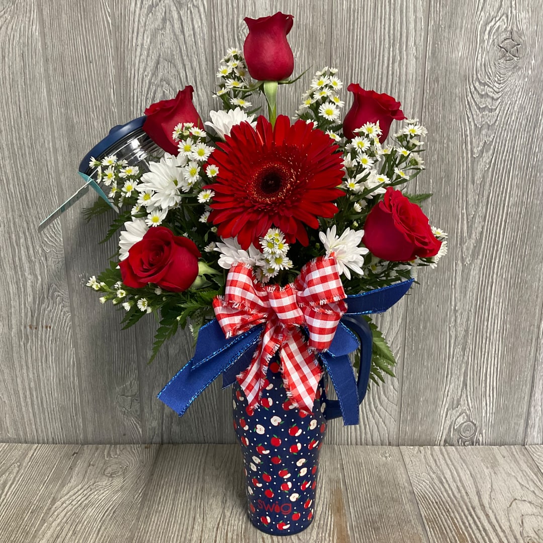Red roses and daisies arranged in a patterned tumbler with a ribbon bow
