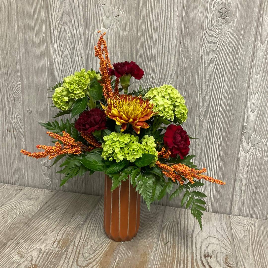 Mixed floral arrangement in a tall orange vase with green and red blooms