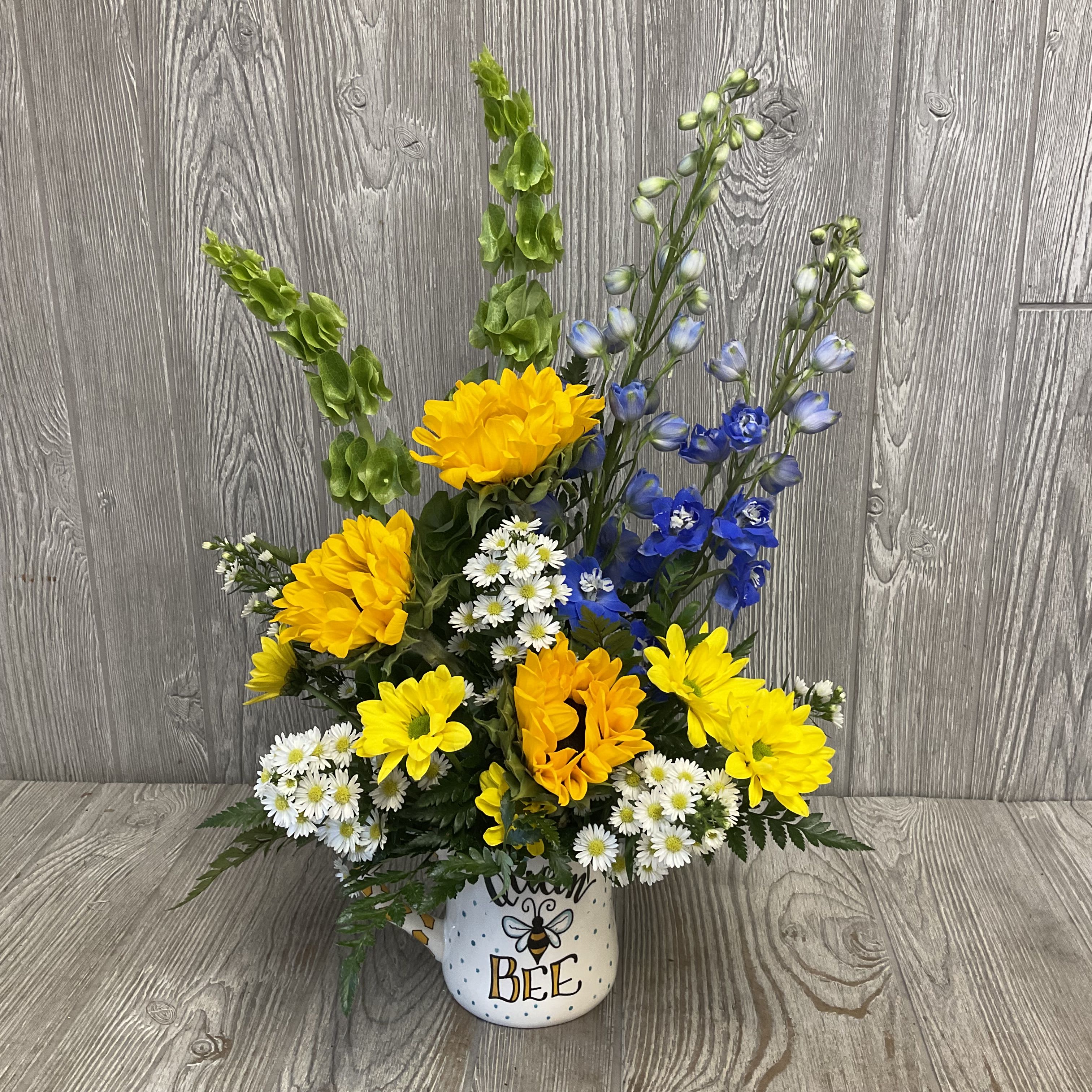 Yellow and blue flowers arranged in a bee-themed mug