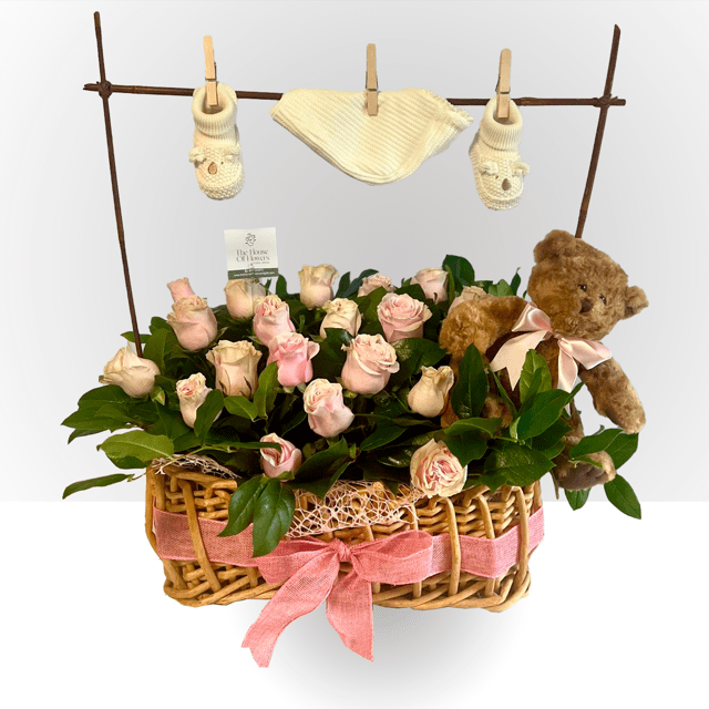 Basket of pale pink roses with a teddy bear and baby booties hanging above on a clothesline