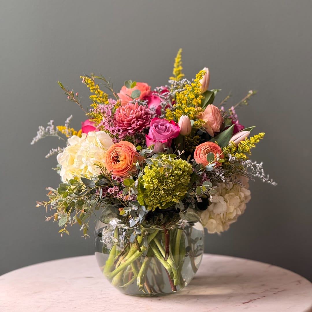 Mixed bouquet in a clear glass vase with pink, peach, white, and yellow blooms