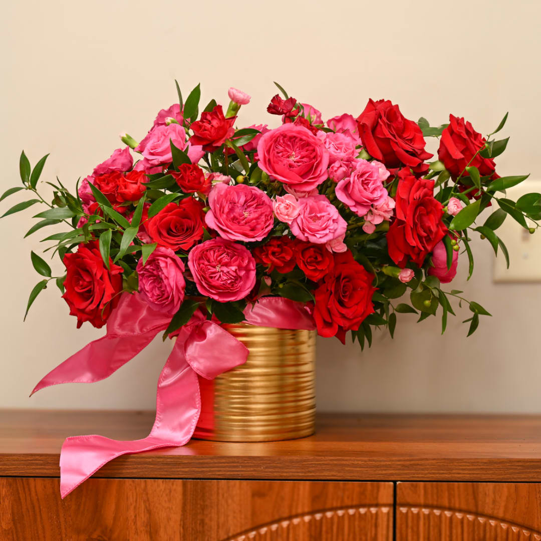 Pink and red roses arranged in a gold tin with a pink ribbon