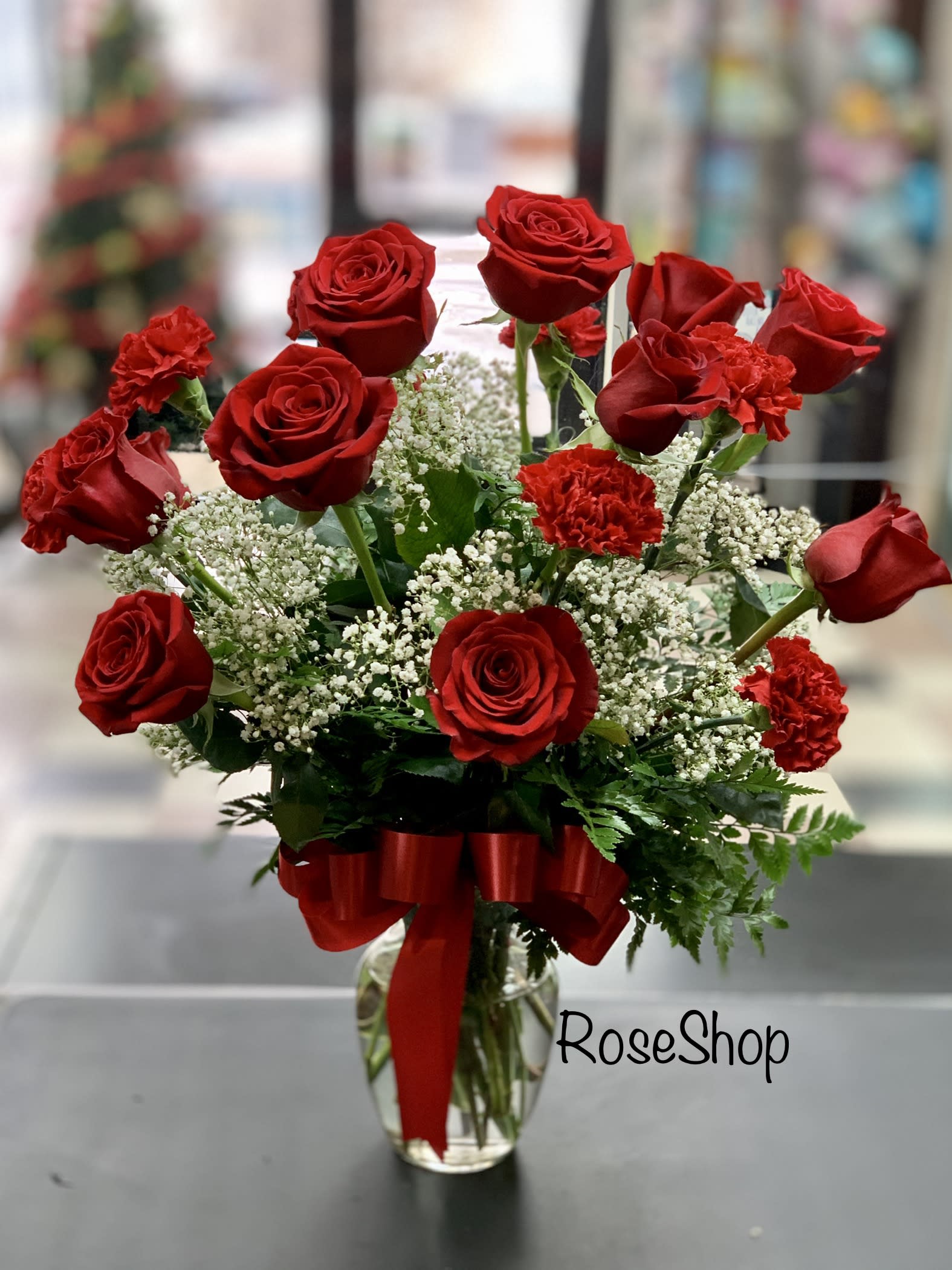 Red roses and carnations arranged in a glass vase with a red ribbon