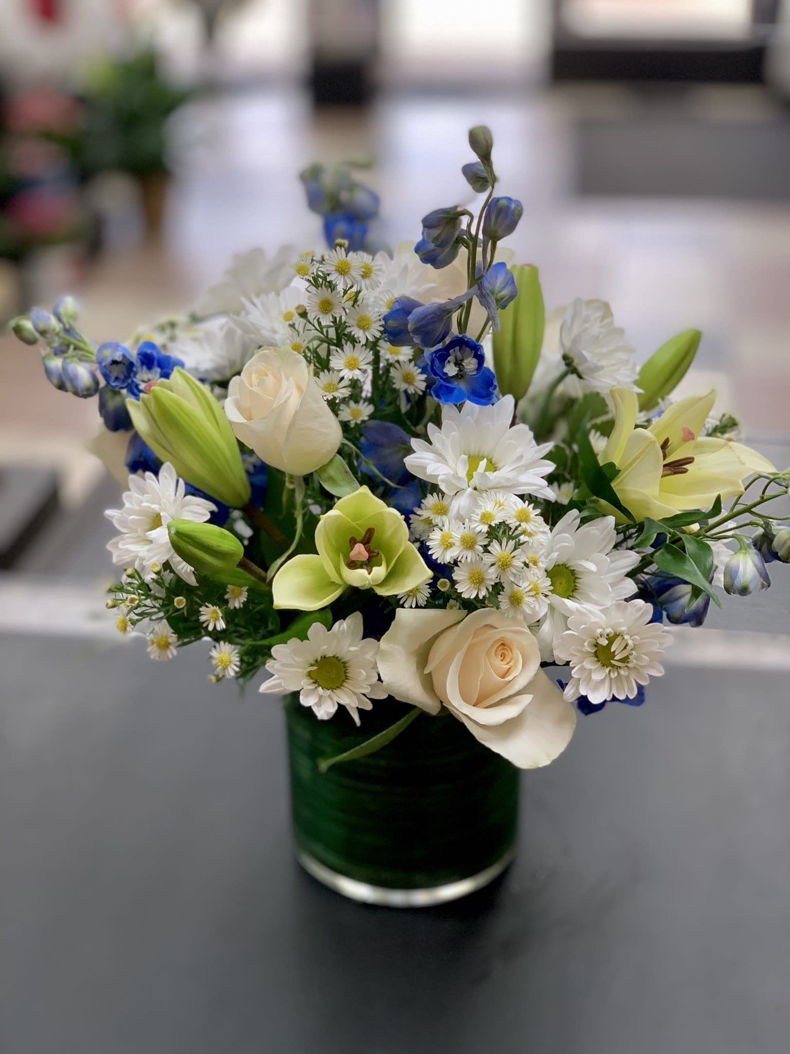 Bouquet of white daisies, cream roses, and blue flowers in a glass vase