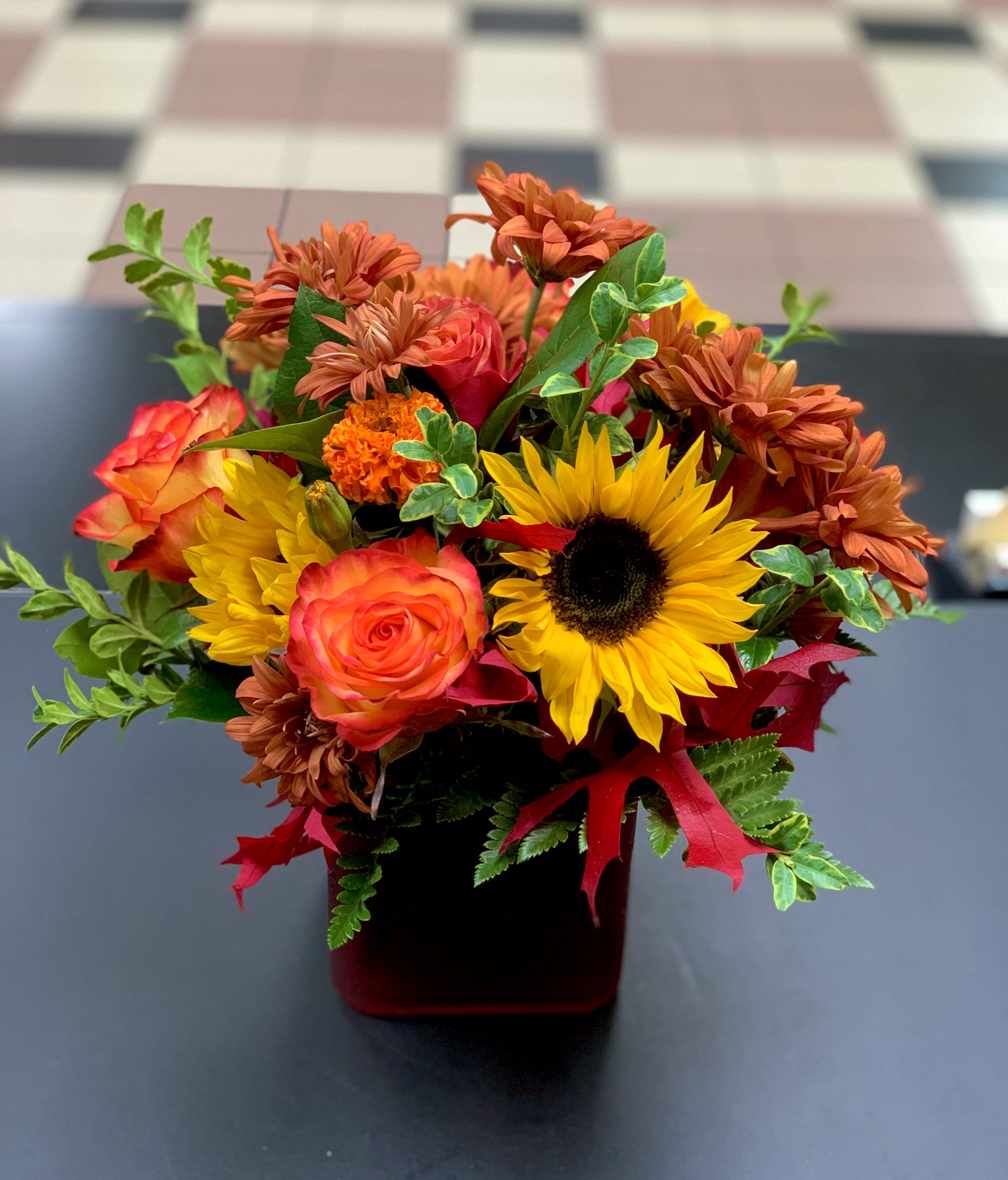 Bouquet of sunflowers, orange roses, and mums in a red vase
