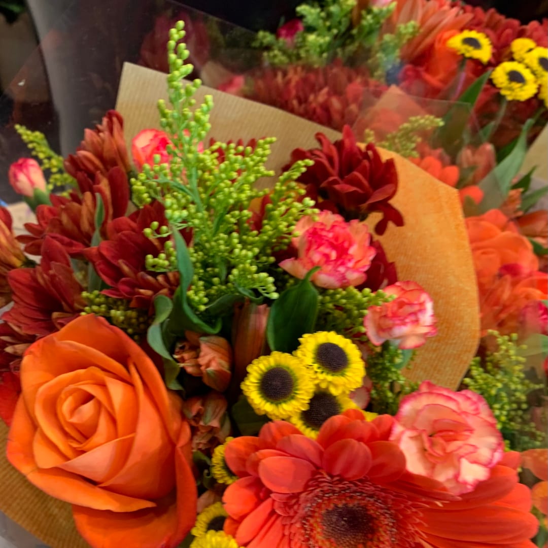 Bouquet of orange and red flowers with yellow accents wrapped in paper