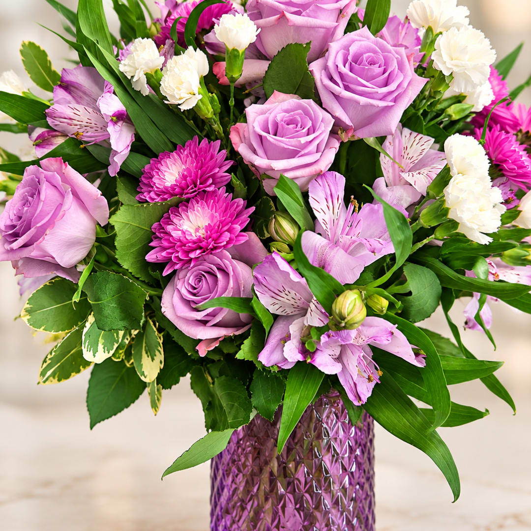 Lavender roses and pink flowers arranged in a purple vase
