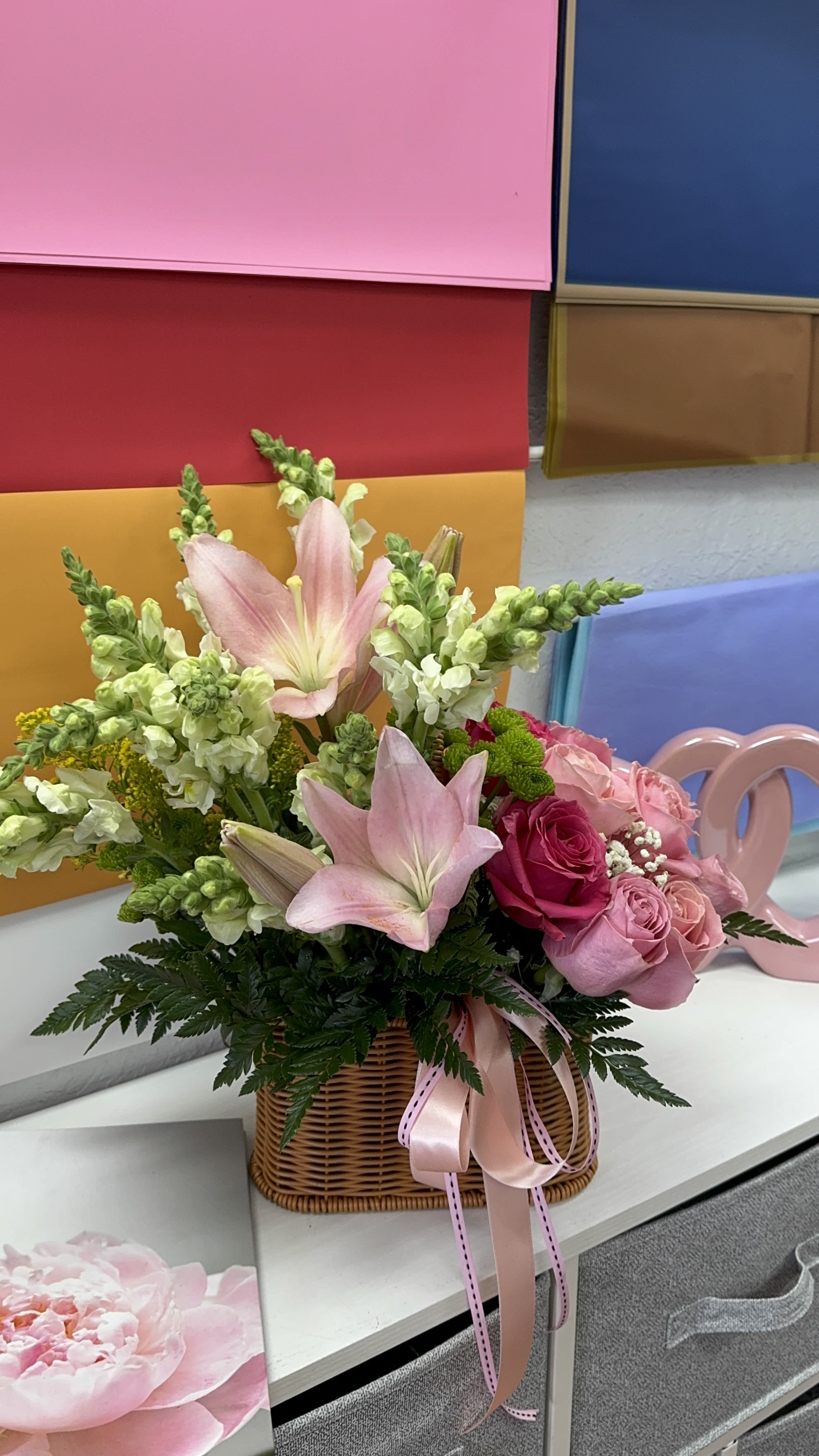 Pink lilies and roses arranged in a wicker basket with ribbon
