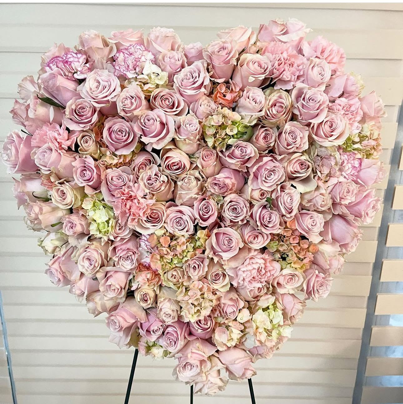 Heart-shaped arrangement of pale pink roses and carnations on an easel
